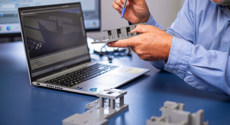 Profissional da Cardan Engenharia analisa modelo físico de construção ao lado de um computador com software de metodologia BIM em exibição na tela