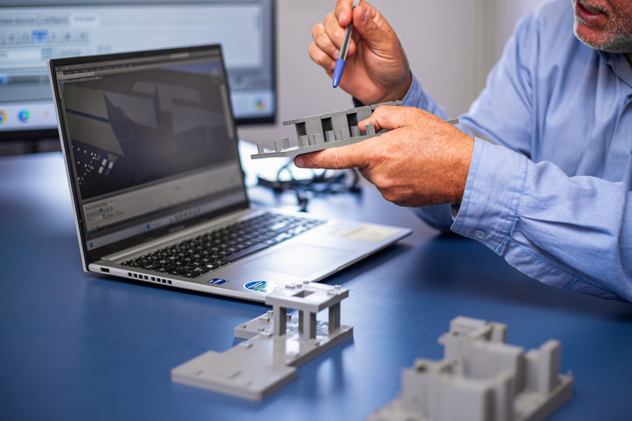 Profissional da Cardan Engenharia analisa modelo físico de construção ao lado de um computador com software de metodologia BIM em exibição na tela