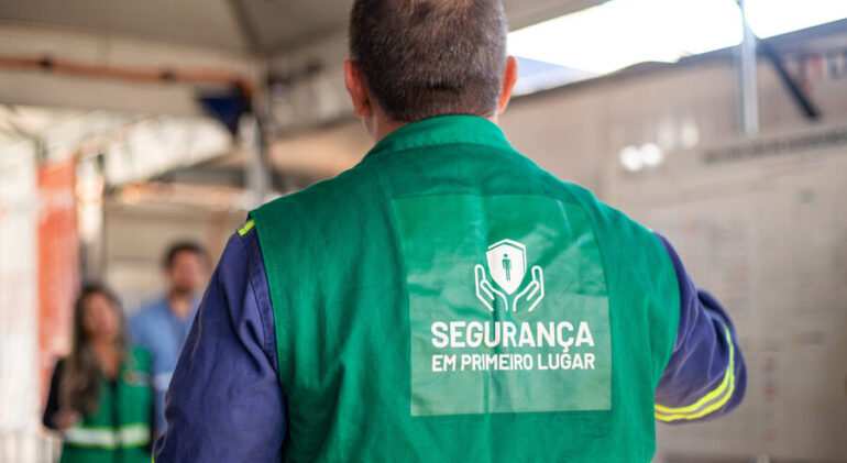 Colaborador com colete escrito “Segurança em primeiro lugar” durante briefing de segurança do trabalho na construção civil.